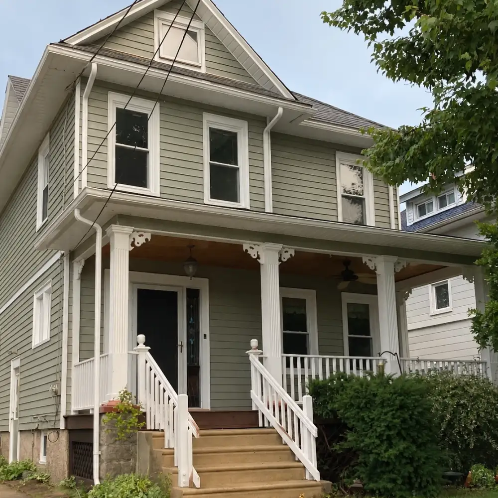 The same house after exterior painting with fresh sage siding and crisp white porch trim