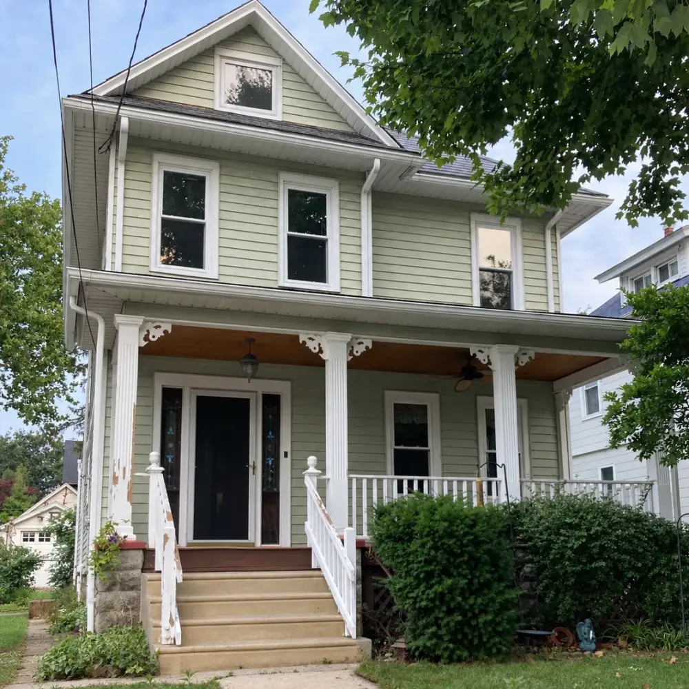 Two-story sage green house with peeling paint on the porch columns and railings before exterior painting